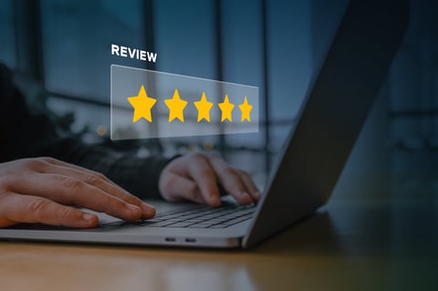 A person using a laptop with a digital overlay of a five-star rating and the word review. Concept of customer feedback, online reputation, business rating